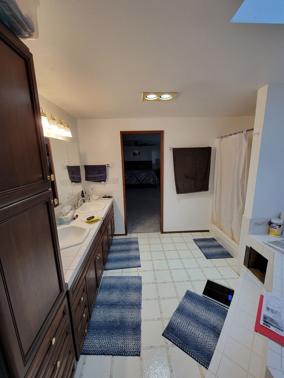Bathroom with a double vanity, blue rugs, and a doorway leading to a bedroom.