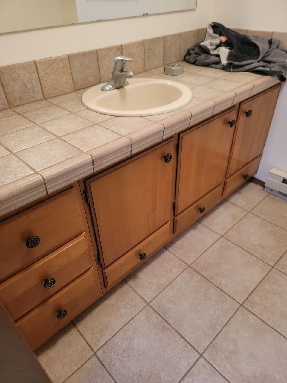 Bathroom with light wood cabinets, beige tile countertop, and sink.