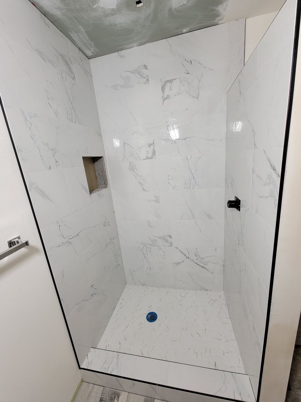 A finished white tiled shower with black trim and a built-in niche.
