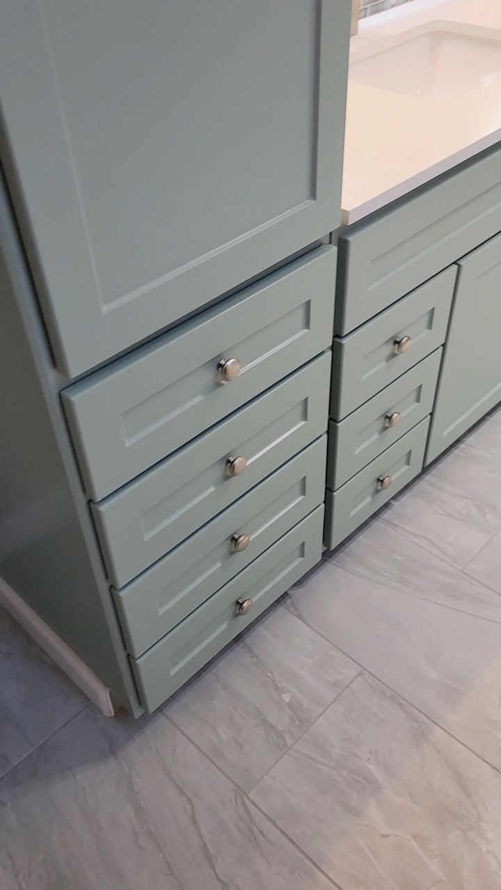 Pale green kitchen cabinets with silver drawer pulls, set on gray tiled floor.