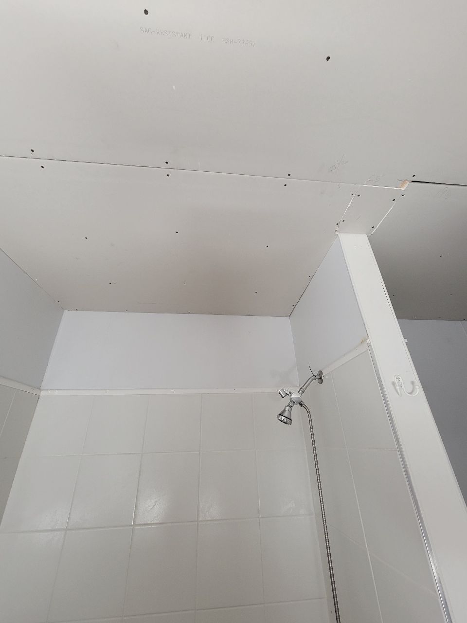 White shower stall with a showerhead on a tiled wall and a cracked ceiling.