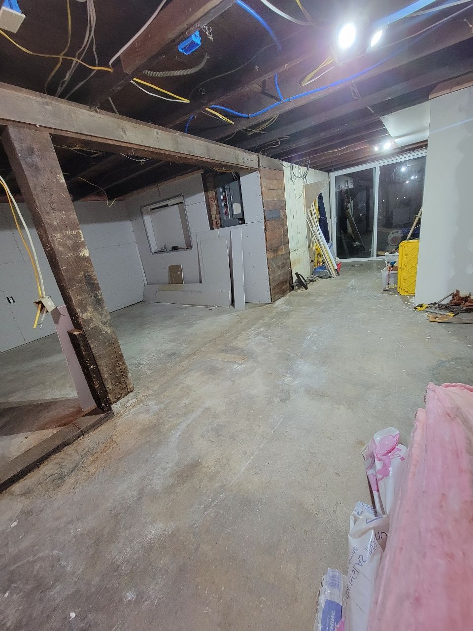 Interior under construction: exposed beams, unfinished walls, concrete floor, large windows.