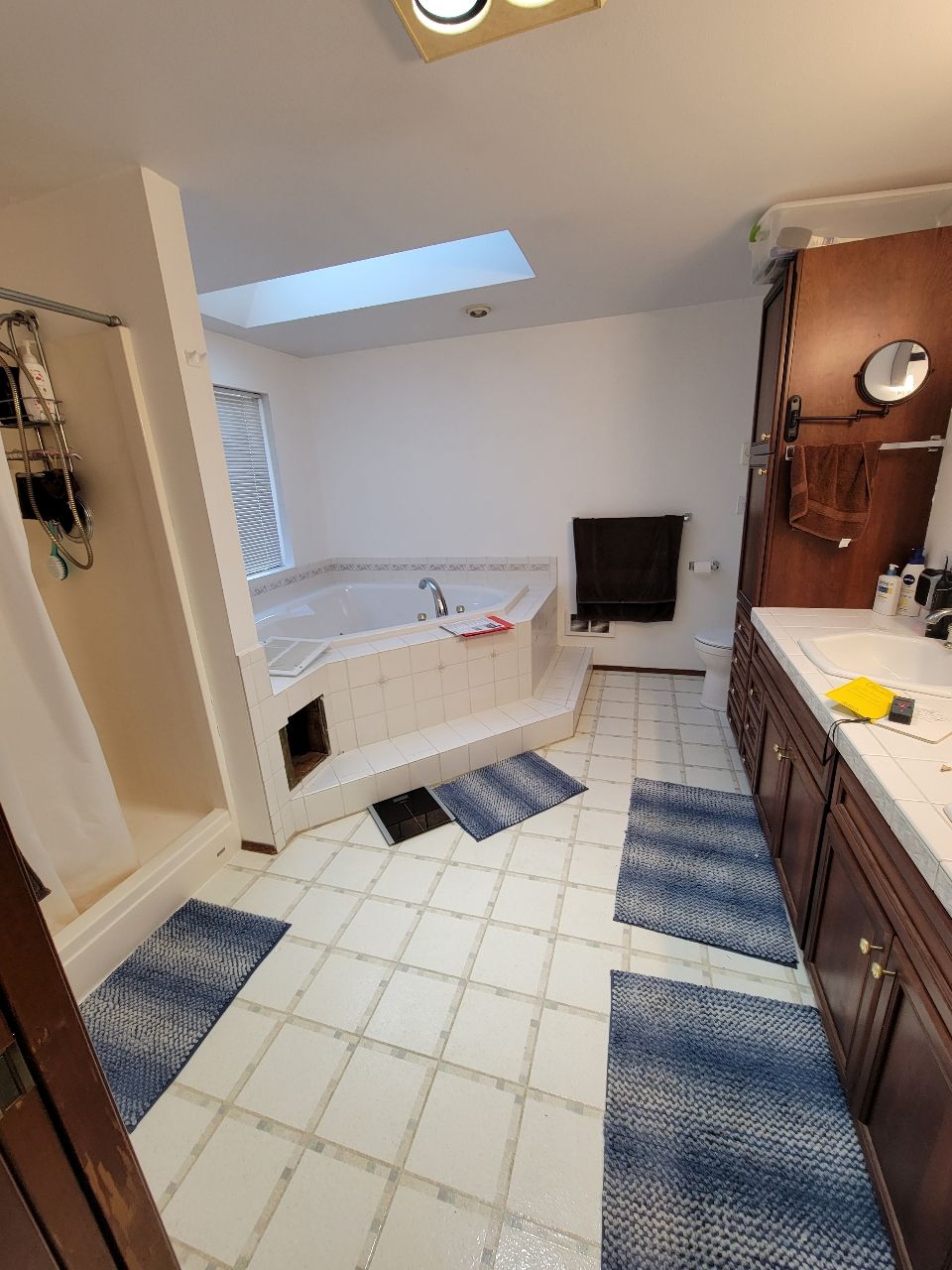 Bathroom with jacuzzi, shower, dark wood vanity, white tile floor, and blue rugs.