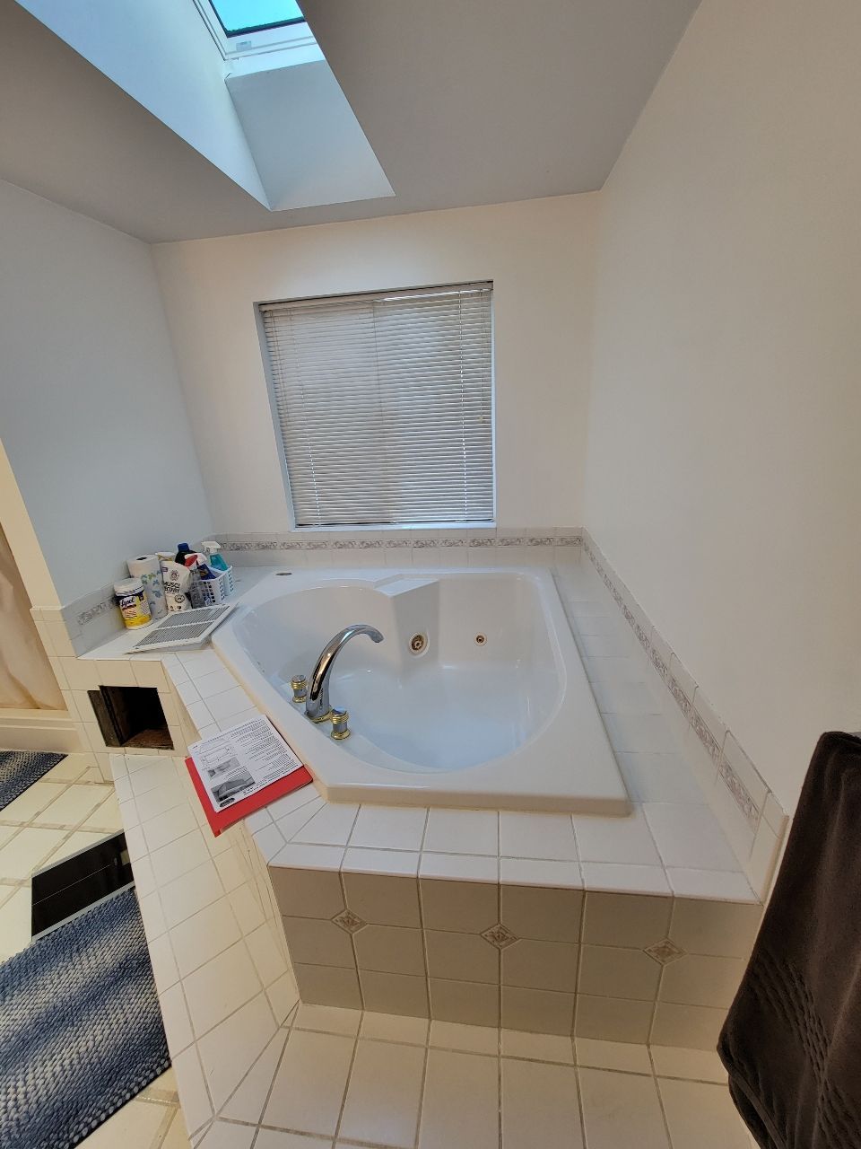 Bathroom with white jacuzzi tub, small window with blinds, and skylight.