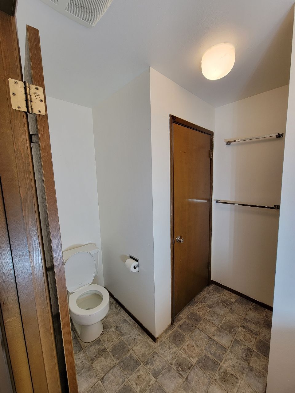Small bathroom with a toilet, closed brown door, and towel racks.
