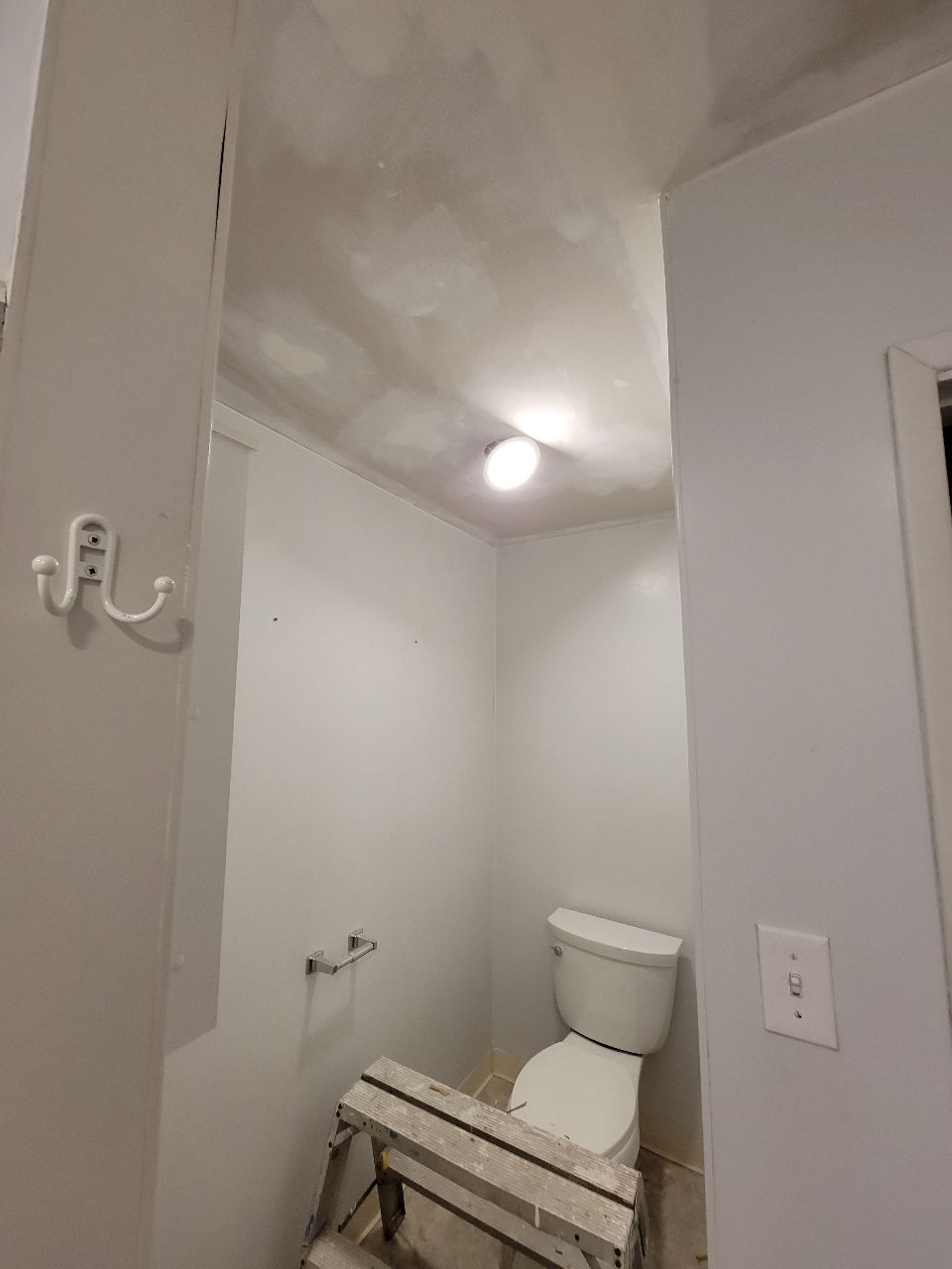 Small, white bathroom with a toilet, light fixture, and step stool.