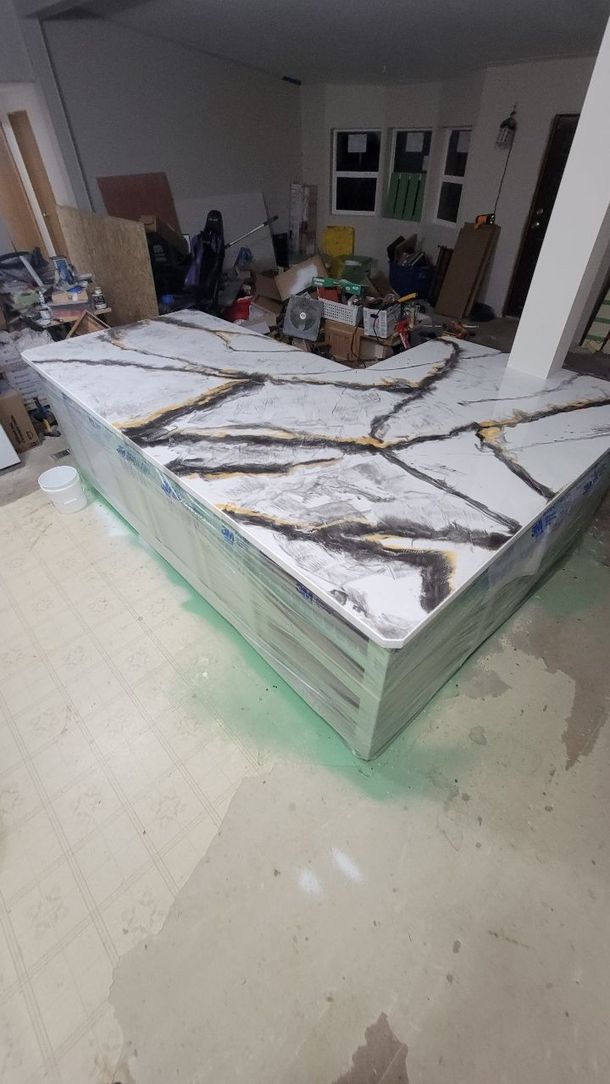 Countertop with white, black, and gold veining, partially covered in protective plastic, in a workshop setting.