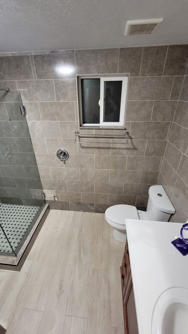 Bathroom with tiled walls, a toilet, vanity, shower, and a small window.