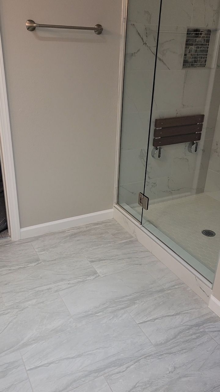 Bathroom with white tile floor, glass shower, and neutral walls.