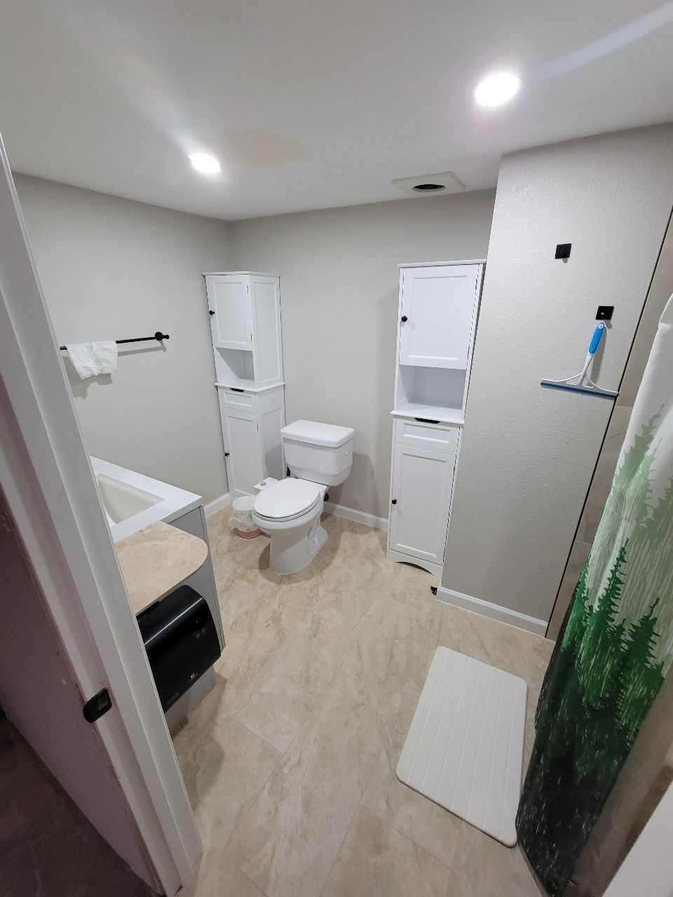 Bathroom with white cabinets, toilet, and shower curtain, light-colored flooring, and neutral walls.