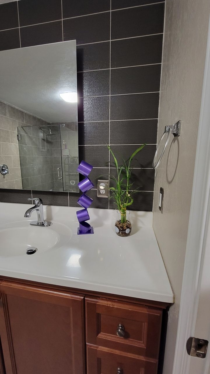Bathroom with a brown cabinet, white countertop, black tiled wall, mirror, and a plant.