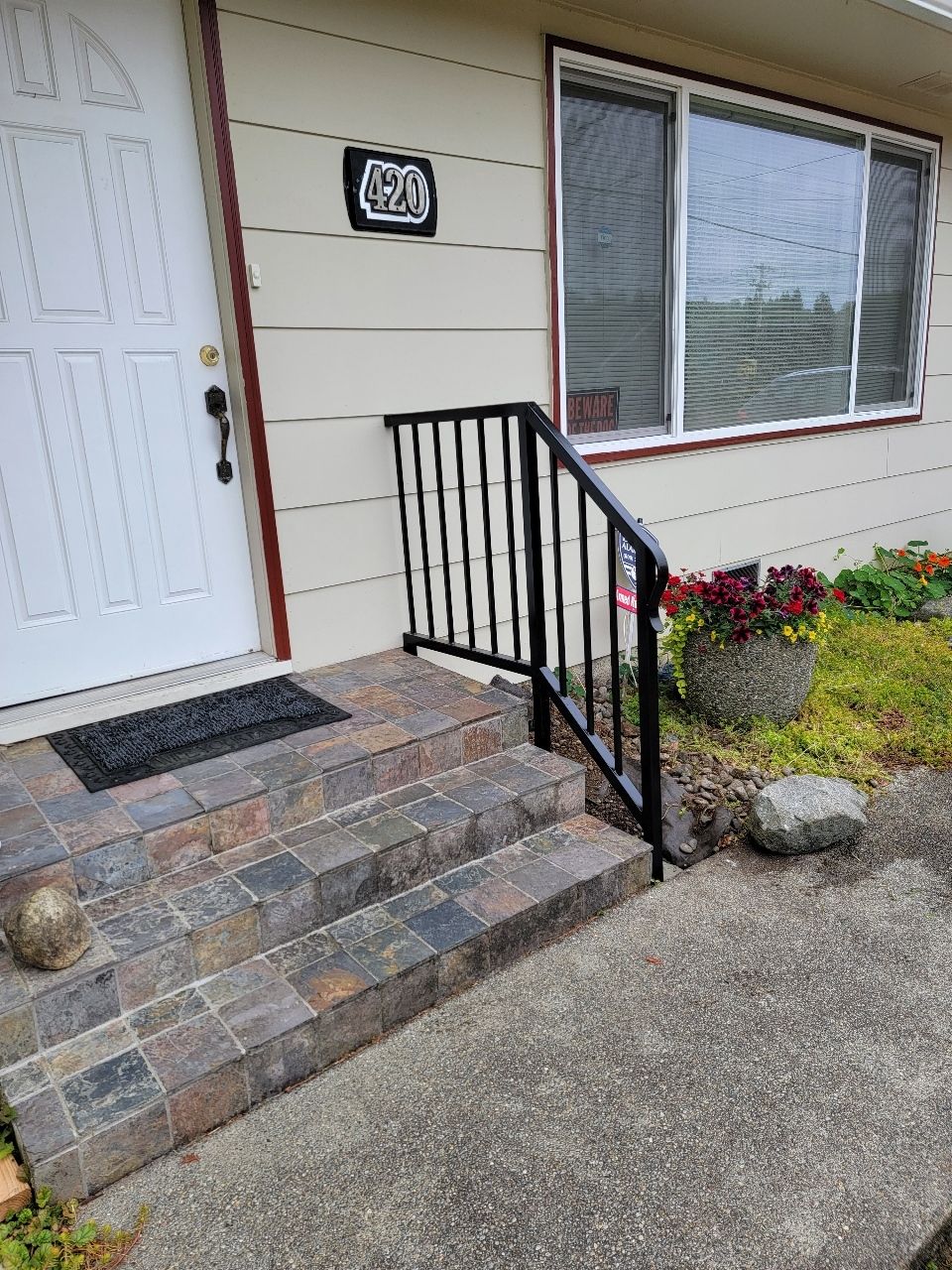Exterior view of a house entrance with steps, a black railing, and a welcome mat.