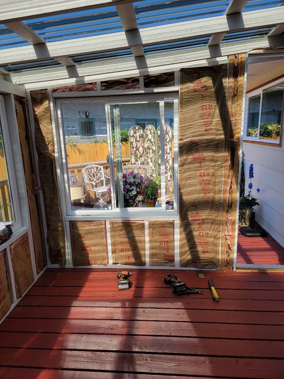 Sunroom construction: insulation installed in wall frames, window in middle, red painted deck.