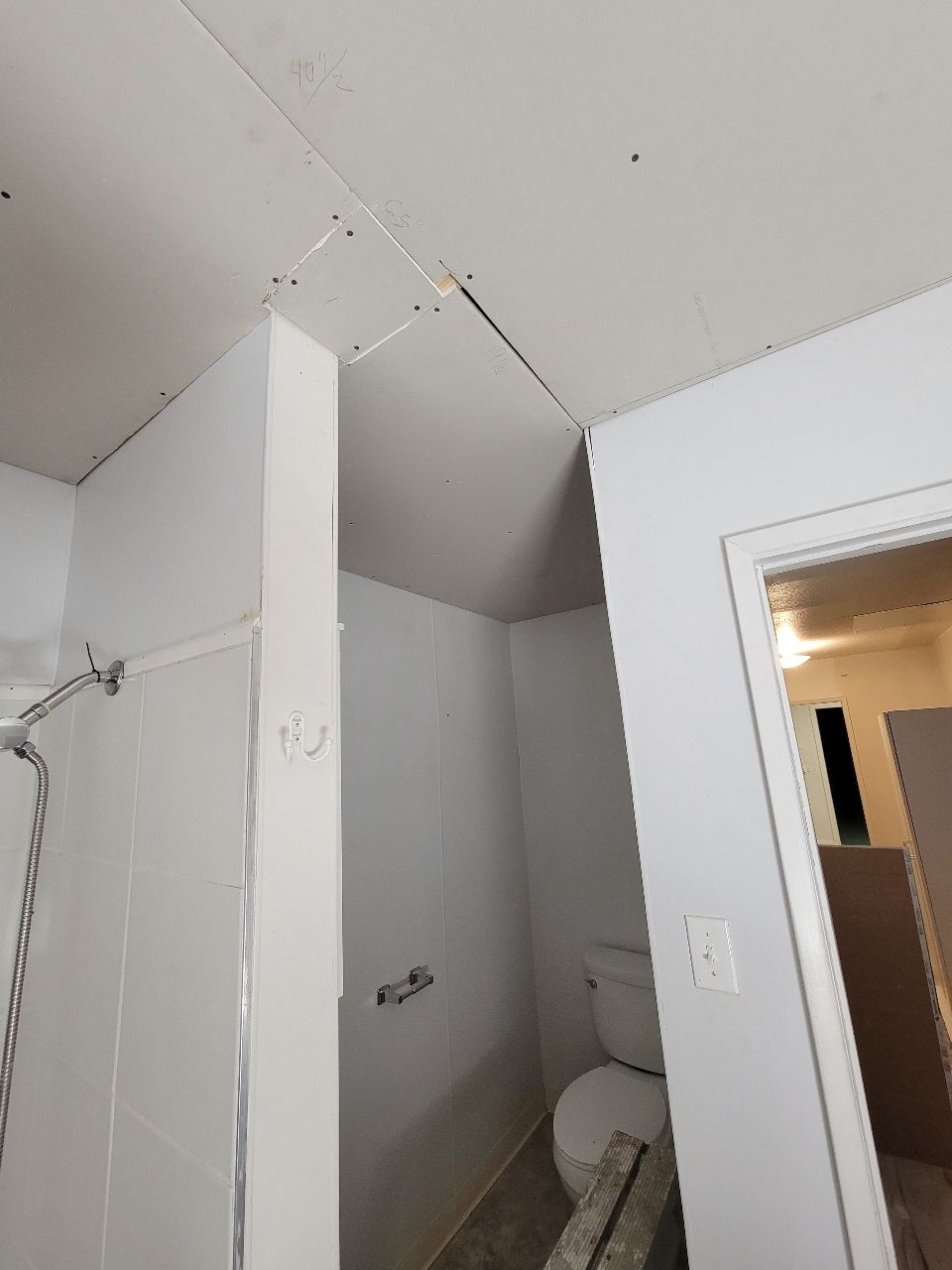 Bathroom renovation in progress, showing unfinished drywall ceiling and walls, with a toilet and shower visible.
