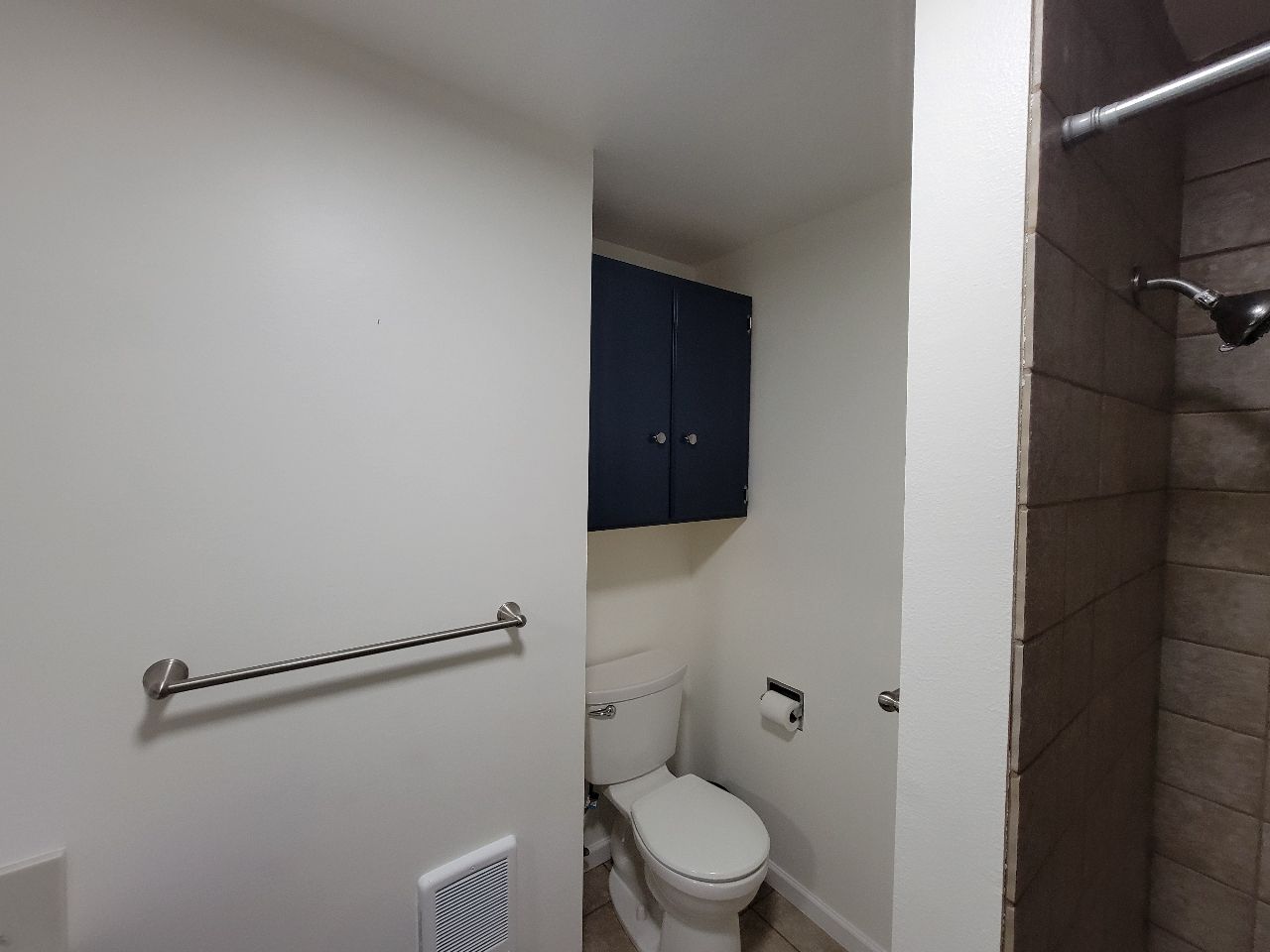 Bathroom with toilet, navy blue cabinet, shower, and towel rack.