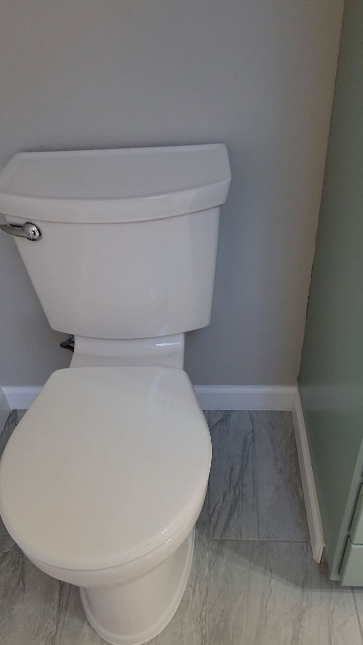 White toilet in a bathroom with gray walls, light gray flooring, and a white baseboard.