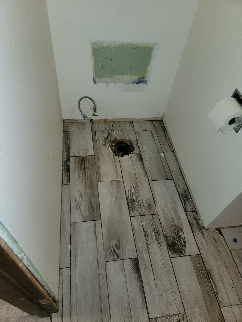 A narrow, tiled bathroom space with a floor drain and exposed plumbing.