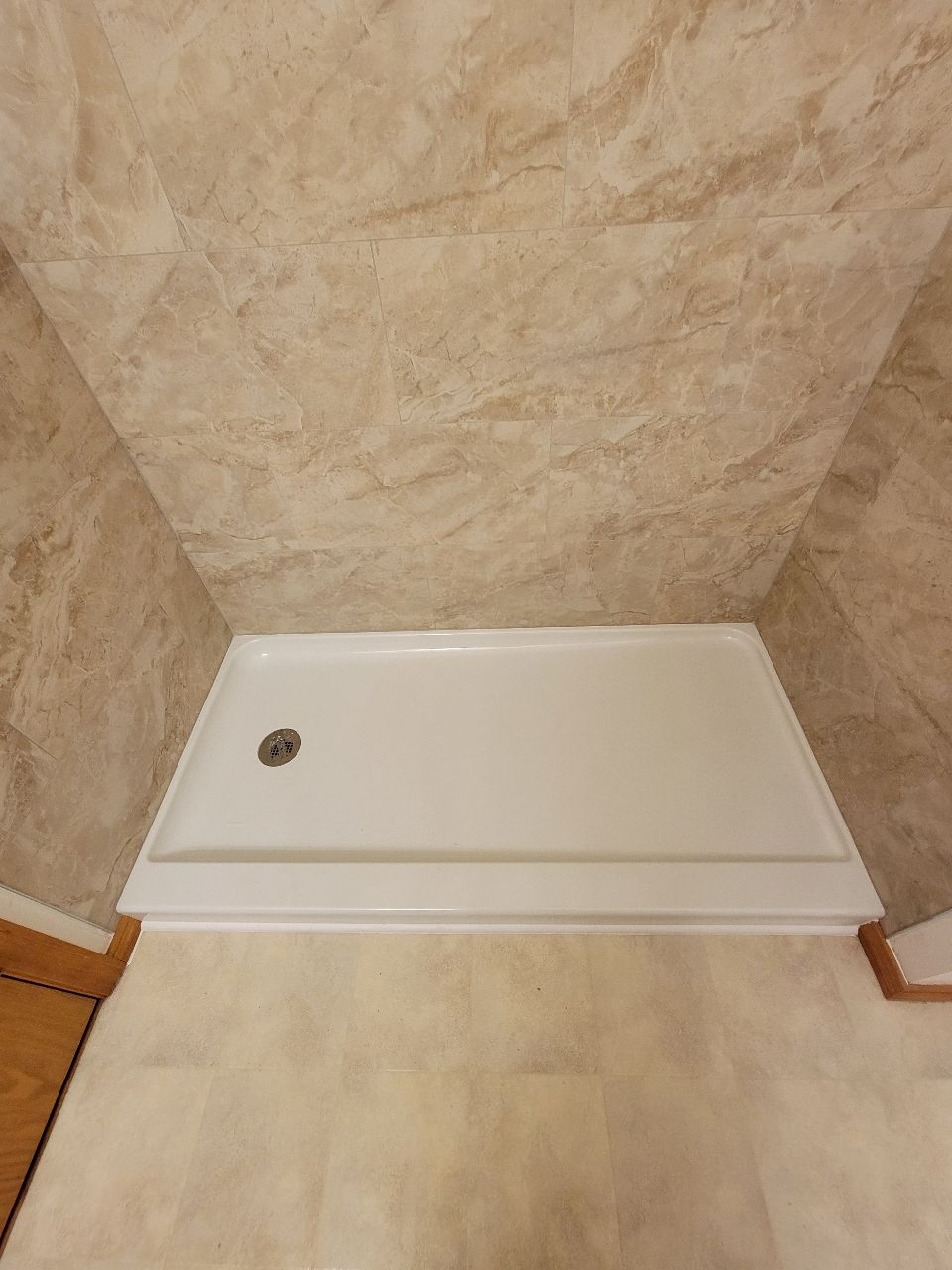 White shower base with drain, surrounded by beige marble-like walls and floor.