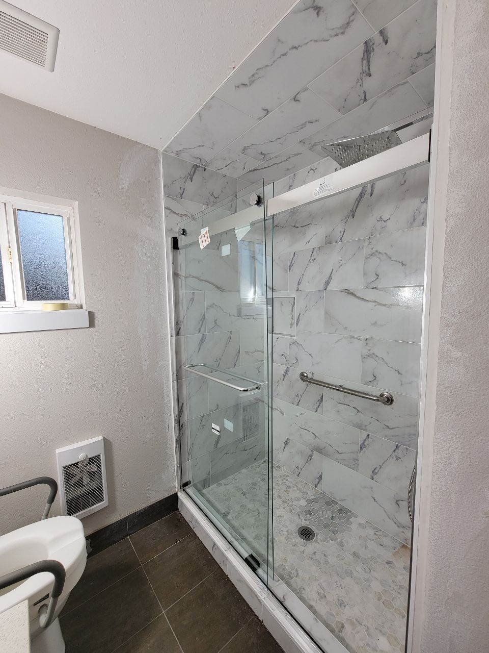 Modern shower with marble-patterned tiles, glass doors, and a silver handle.