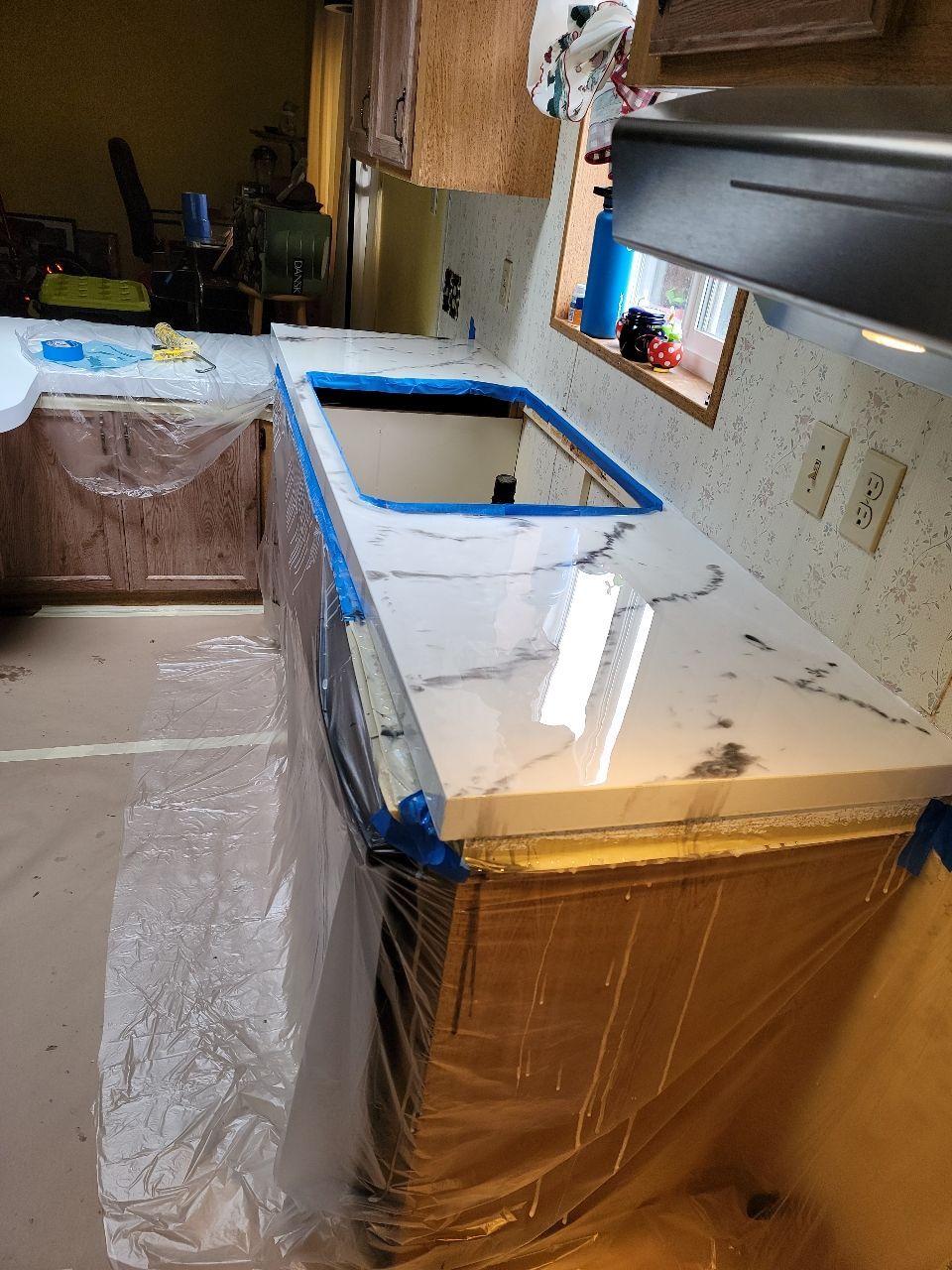 Newly installed white marble-look countertop in a kitchen. Cabinets covered in plastic, sink cutout visible.