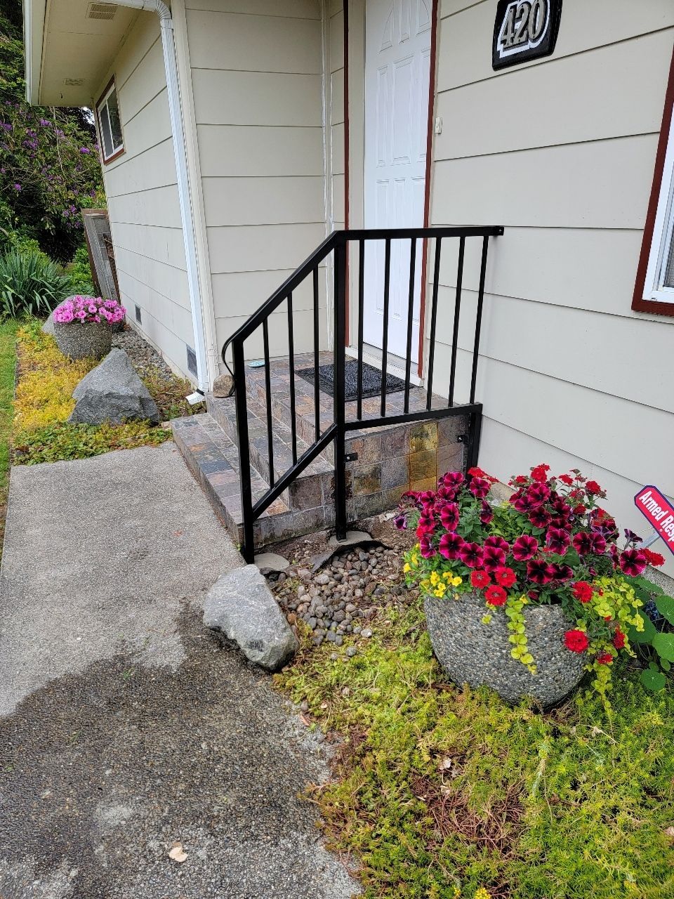 Small house entrance with steps and handrail, flanked by flower pots.