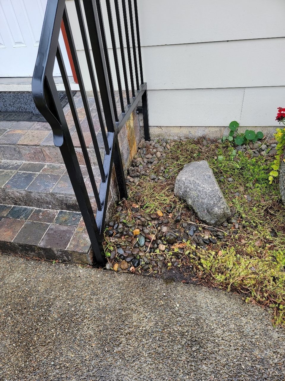 Black metal railing beside stone steps and a gravel bed next to a light-colored building.