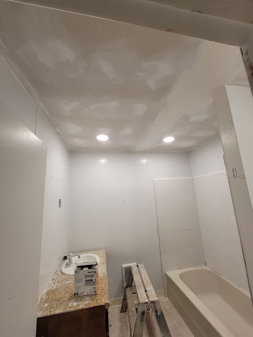 Bathroom with newly painted white walls and ceiling, light fixtures, vanity, and bathtub.