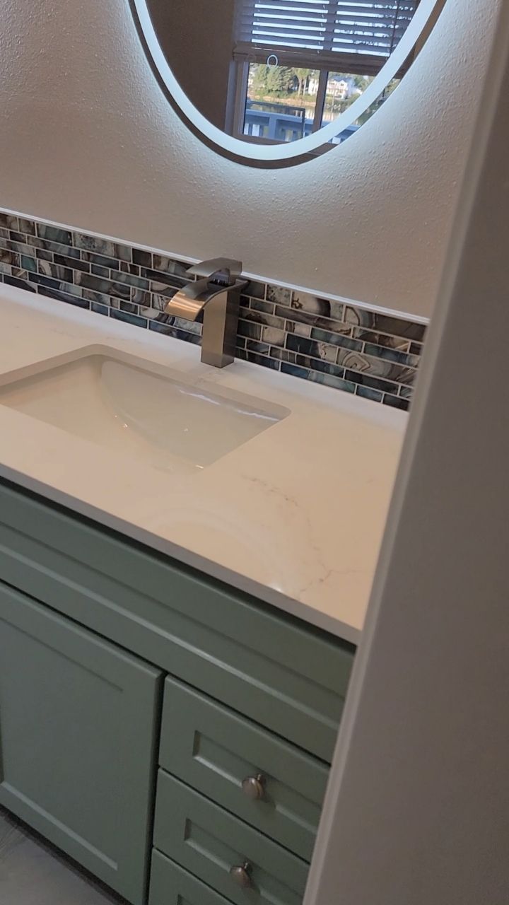 Bathroom vanity with a light green cabinet, white countertop, and a mosaic backsplash.