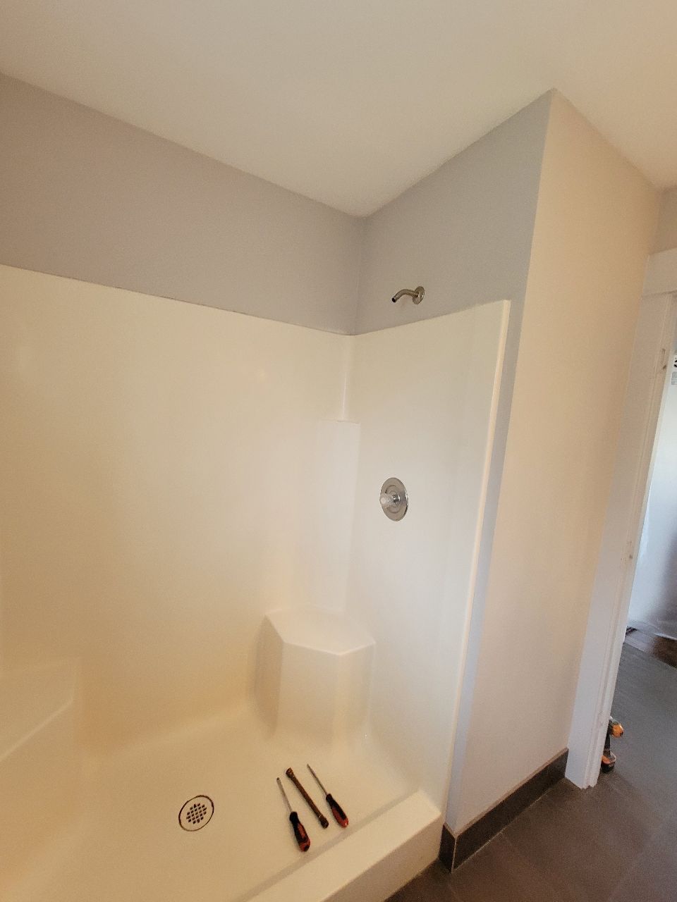 White shower stall with gray walls and a silver faucet. Screwdrivers sit on the shower base.