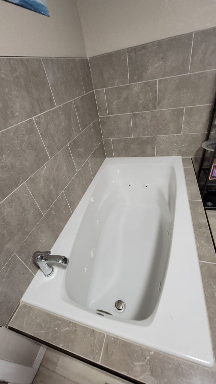 White bathtub with gray tiled walls and surround. Chrome faucet.