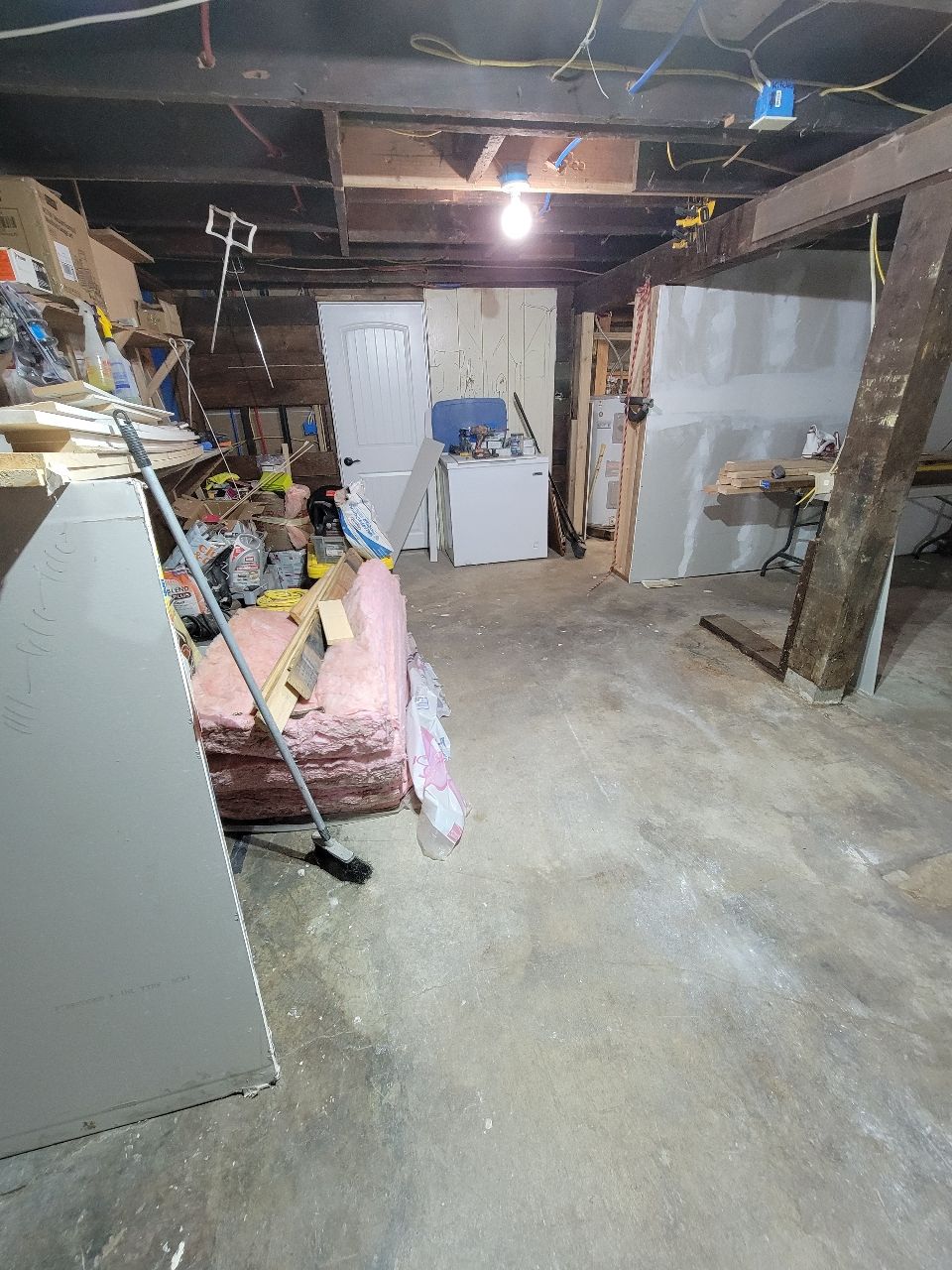 Cluttered basement with insulation, drywall, and unfinished walls. A door and a washing machine are visible.