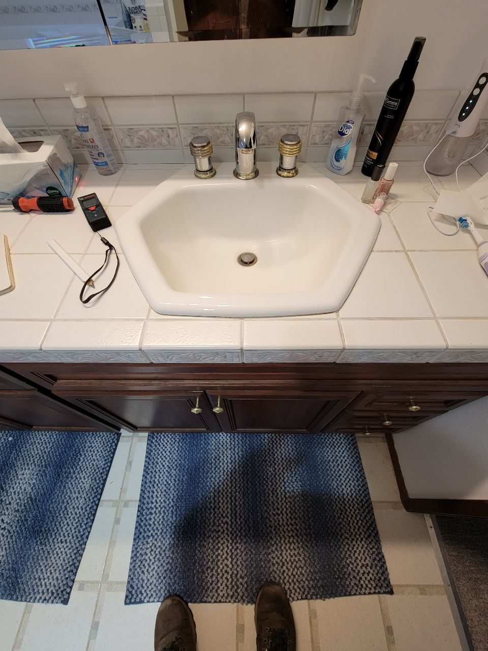 Bathroom sink with faucet, toiletries, and mats. Brown cabinets, white sink and counter.