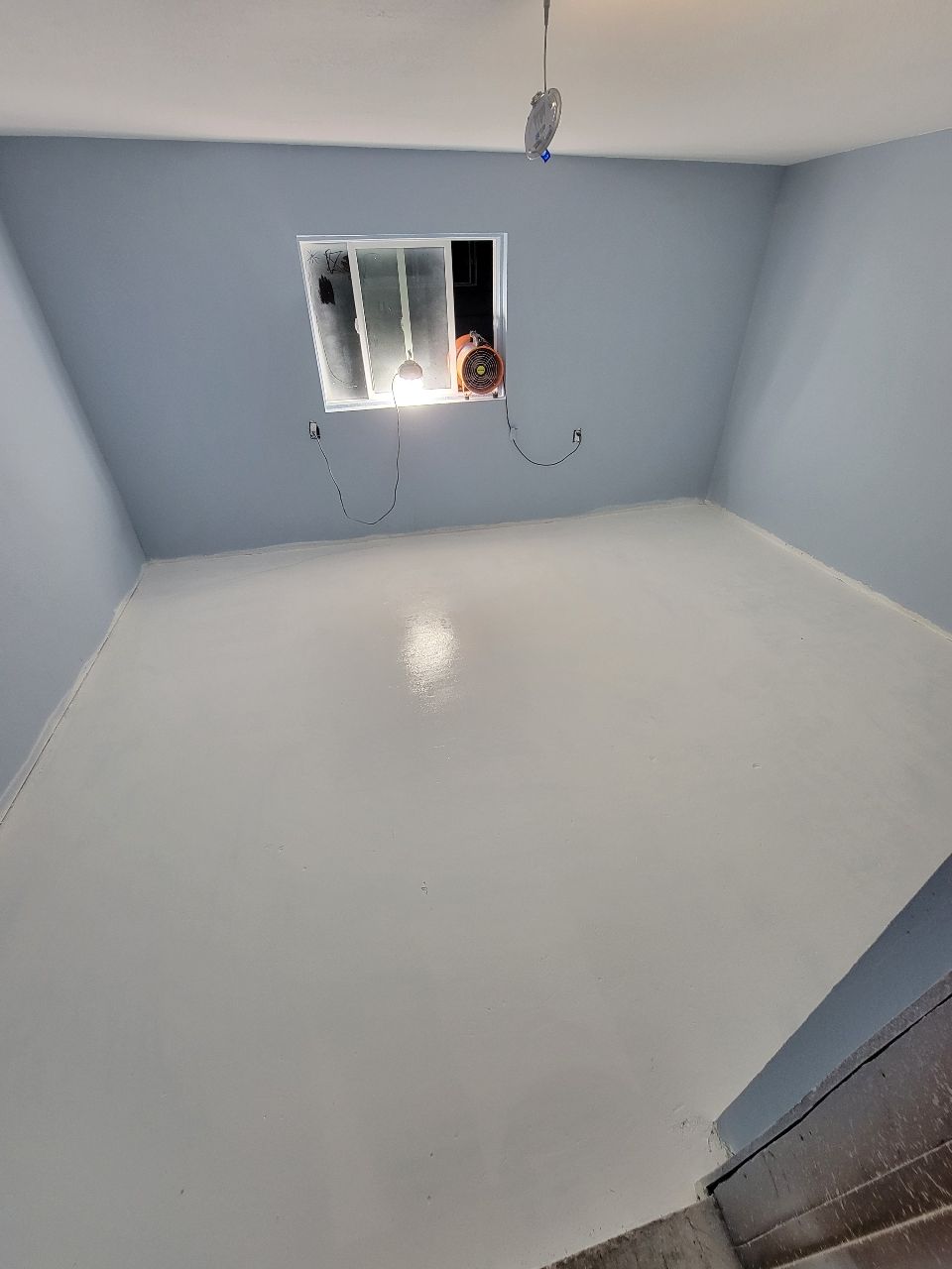 Empty room, light blue walls, white floor, small window with light.