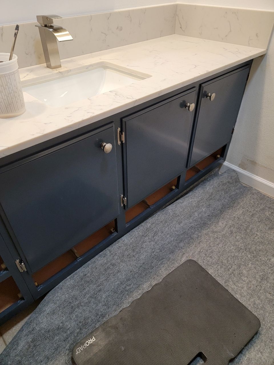 Blue bathroom vanity with white countertop and silver faucet, door open, and knee pad.