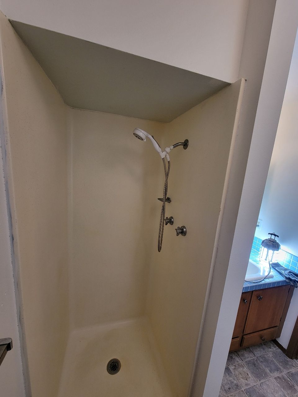 Small shower stall with beige walls, showerhead, and fixtures; corner placement.