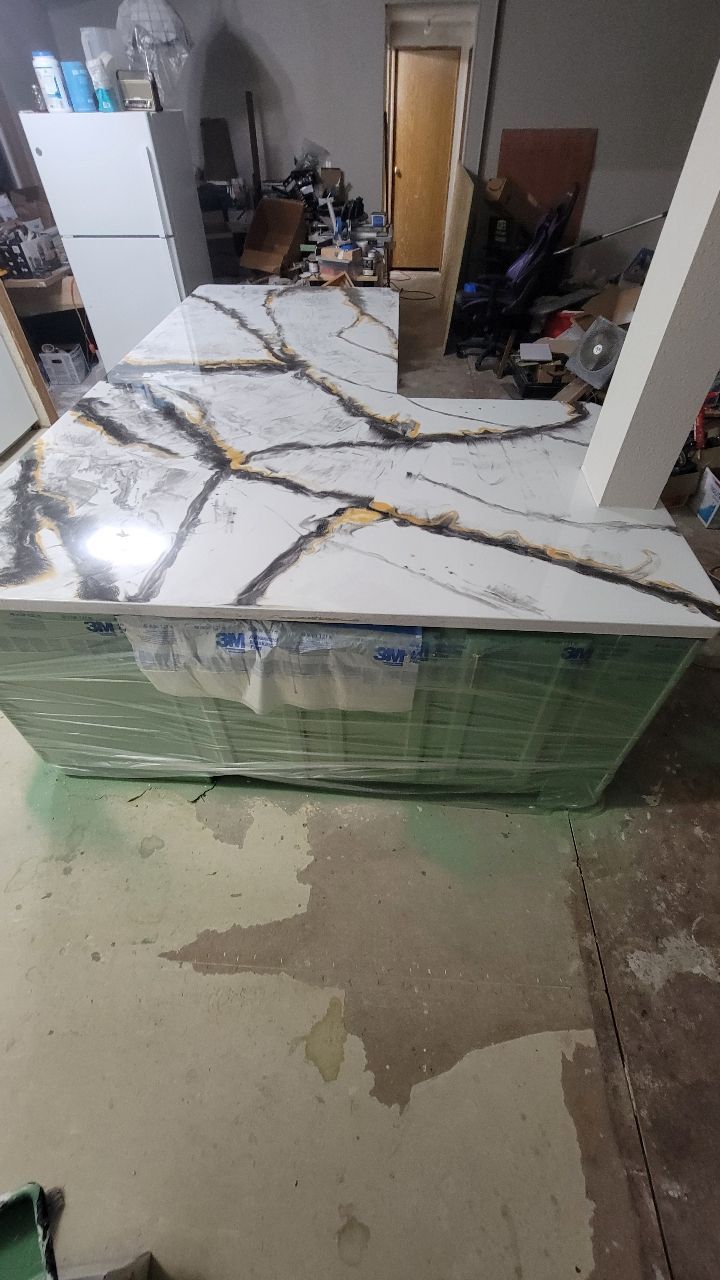 Countertop with marble pattern and gold veining sits atop a green base, in a cluttered interior.