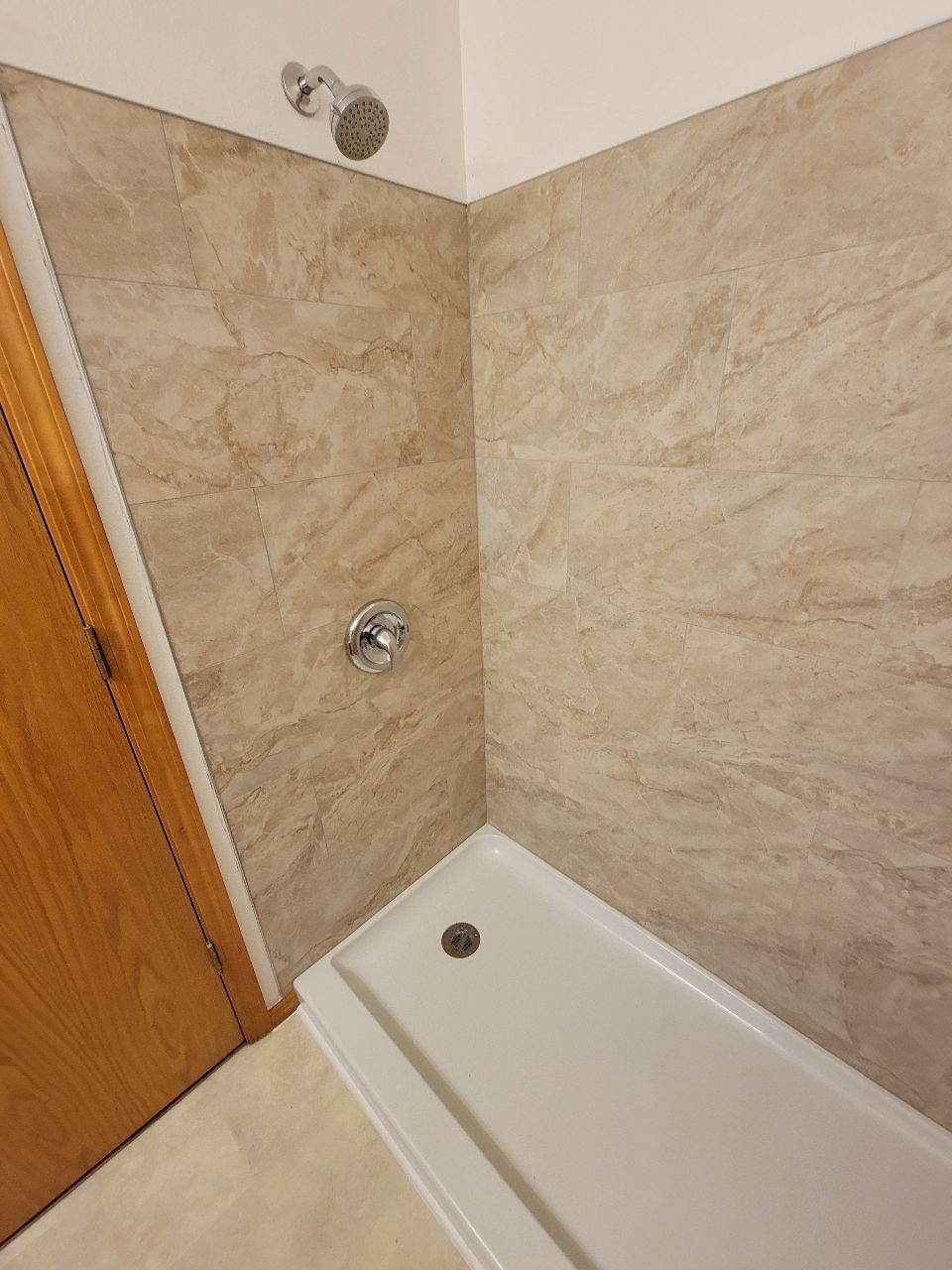 Shower stall with beige marbled walls, white basin, and chrome fixtures.