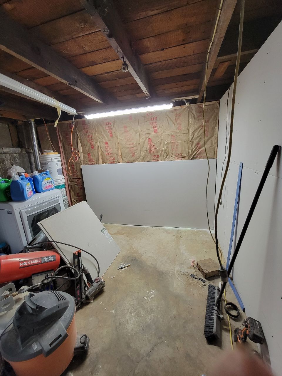 Basement with drywall, insulation, and tools, with a washing machine and a concrete floor.
