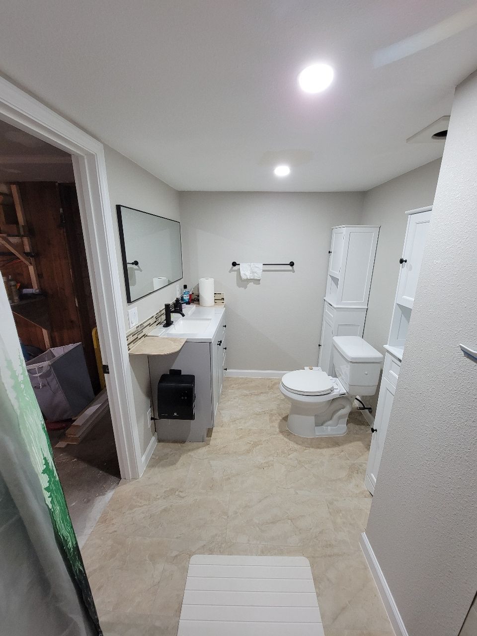 Bathroom with light beige tile, a white toilet, gray vanity, and a large mirror.
