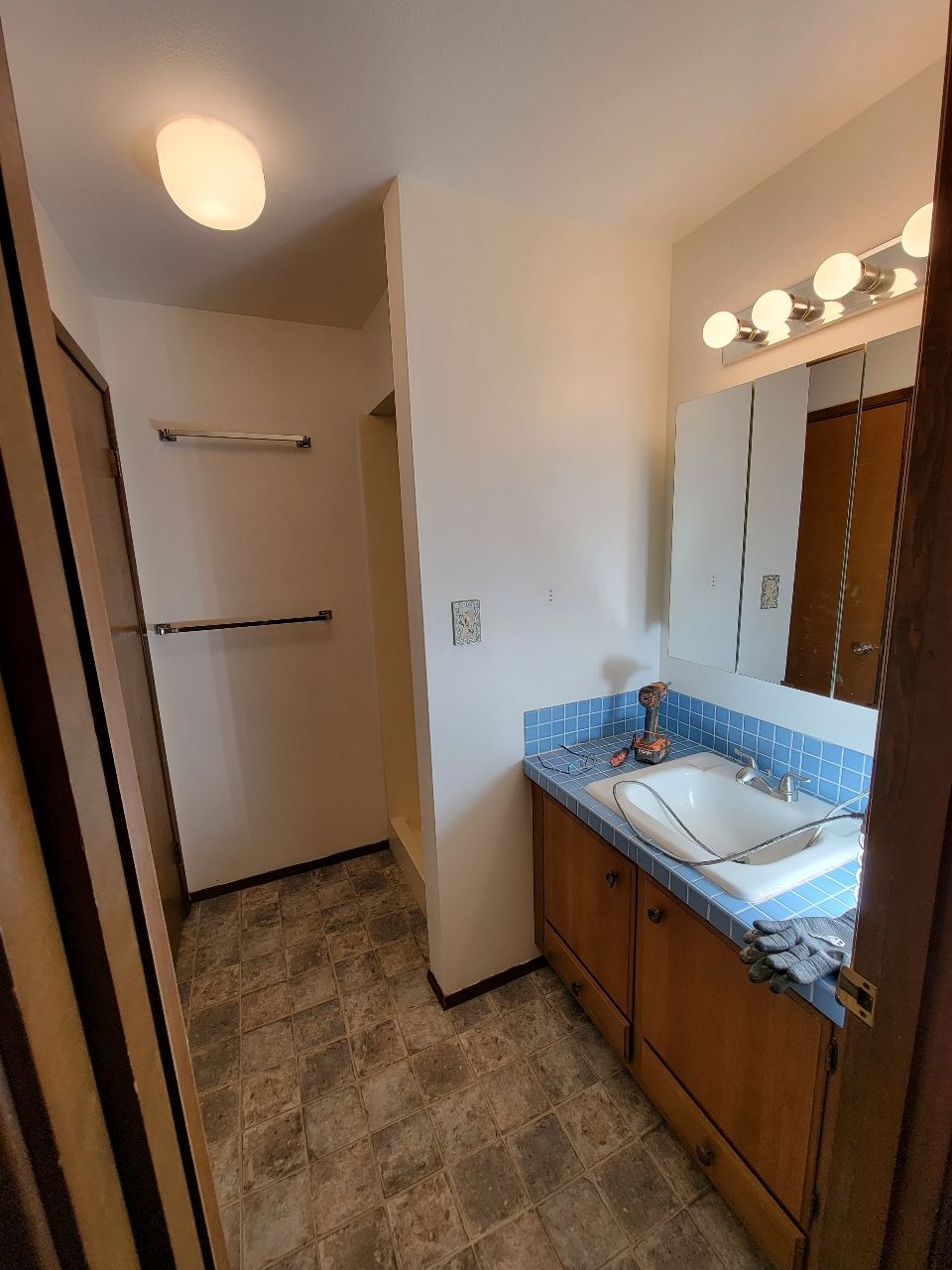 Bathroom with blue tile countertop, wooden cabinets, and a light-colored floor. A walk-in closet is on the left.