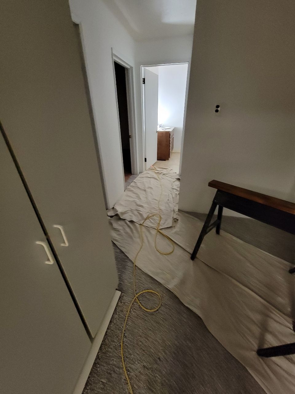 A hallway with drop cloths, a cabinet, and a sawhorse, likely in a room under renovation.