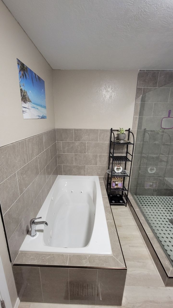 Bathroom with a built-in bathtub, tiled walls, a shower, and a small shelf unit.