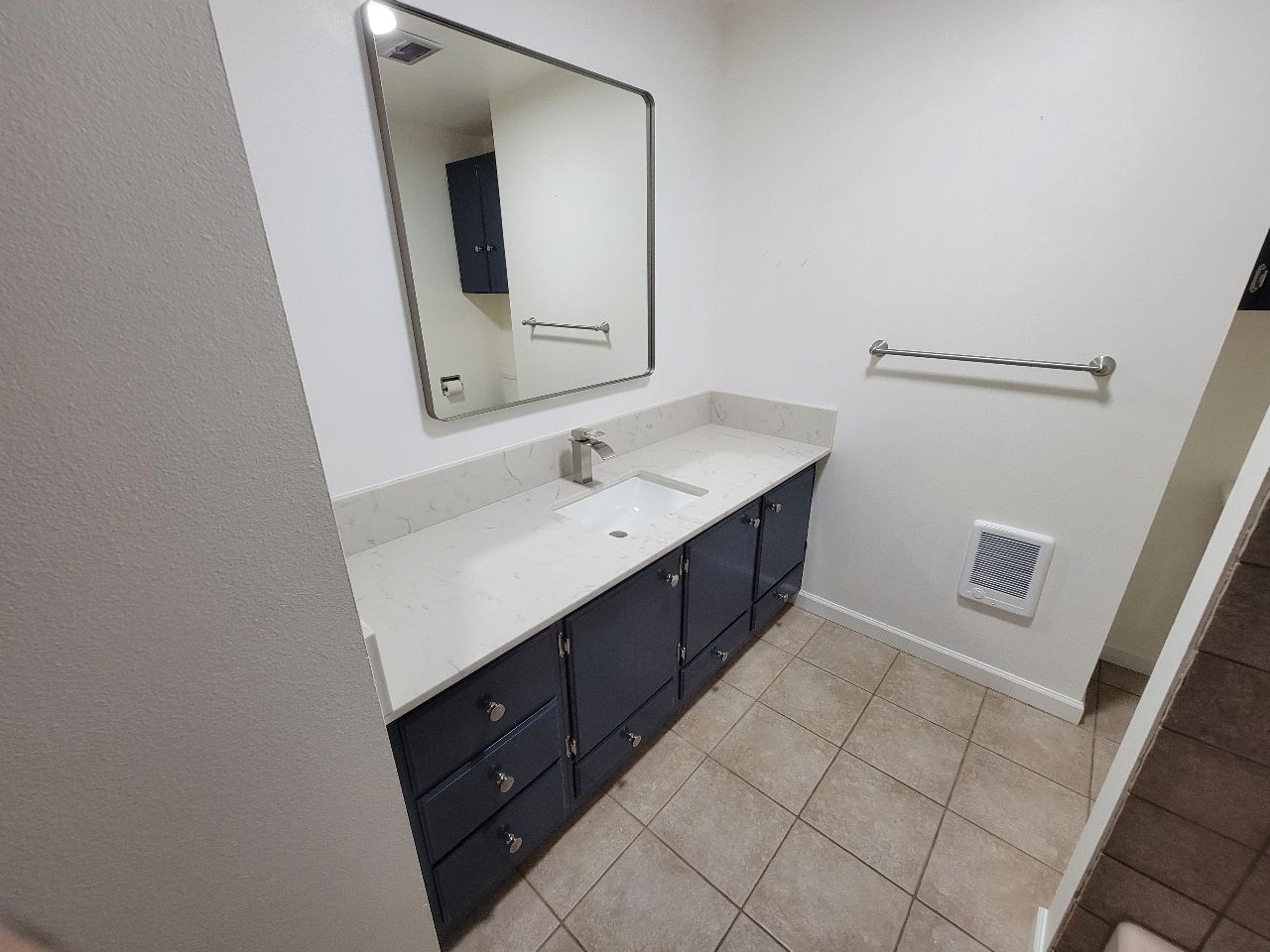 Bathroom with a dark blue vanity, white countertop, and a large mirror.