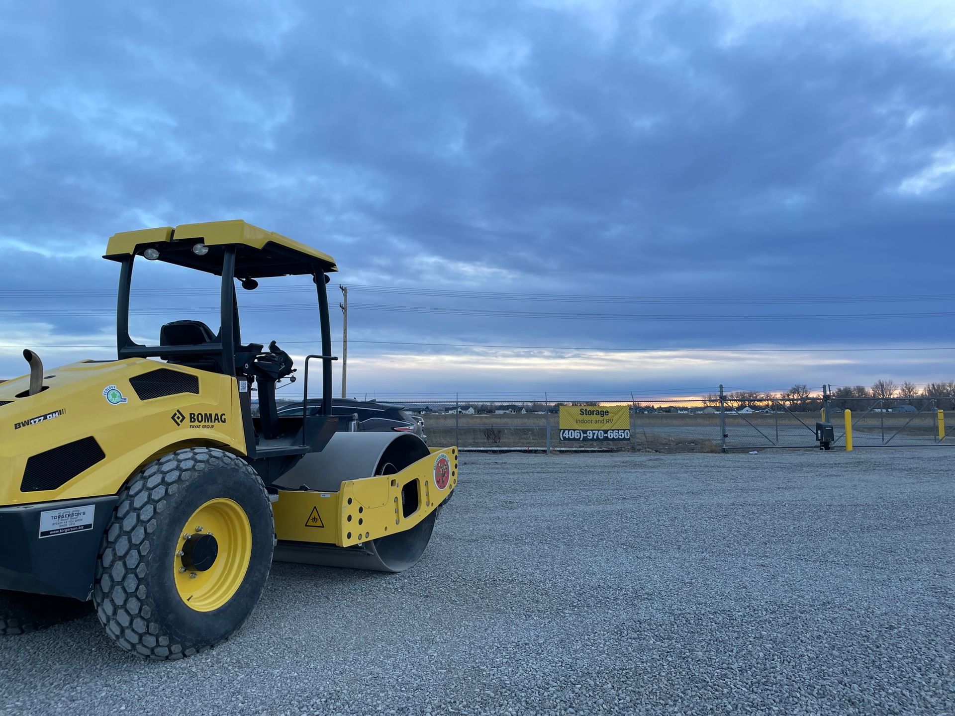 A yellow tractor is parked in a gravel lot.