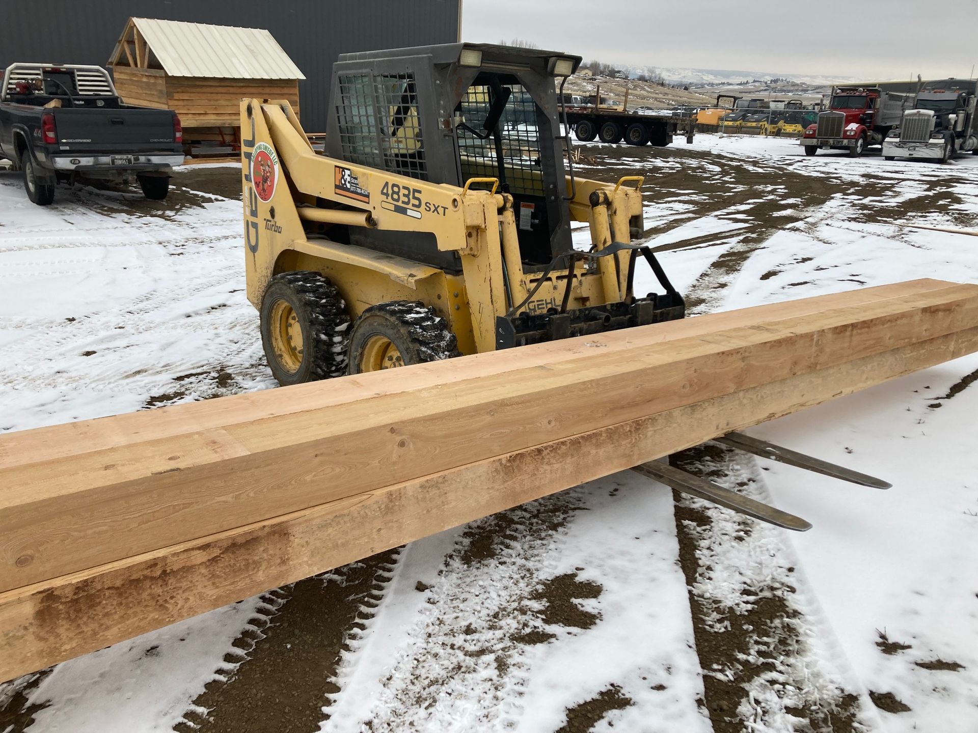A yellow skid steer is carrying a large piece of wood