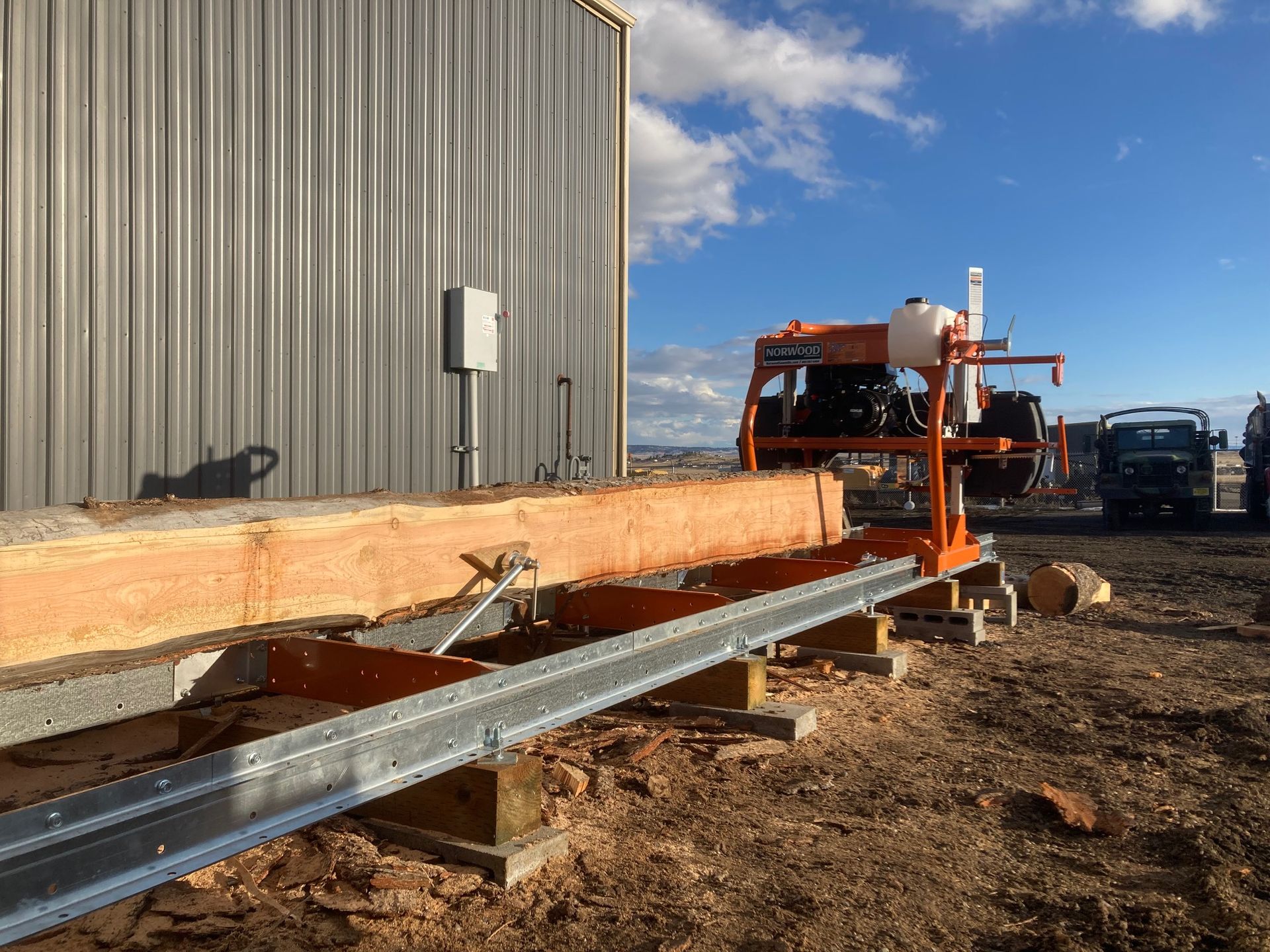 A machine is cutting a piece of wood in front of a building.