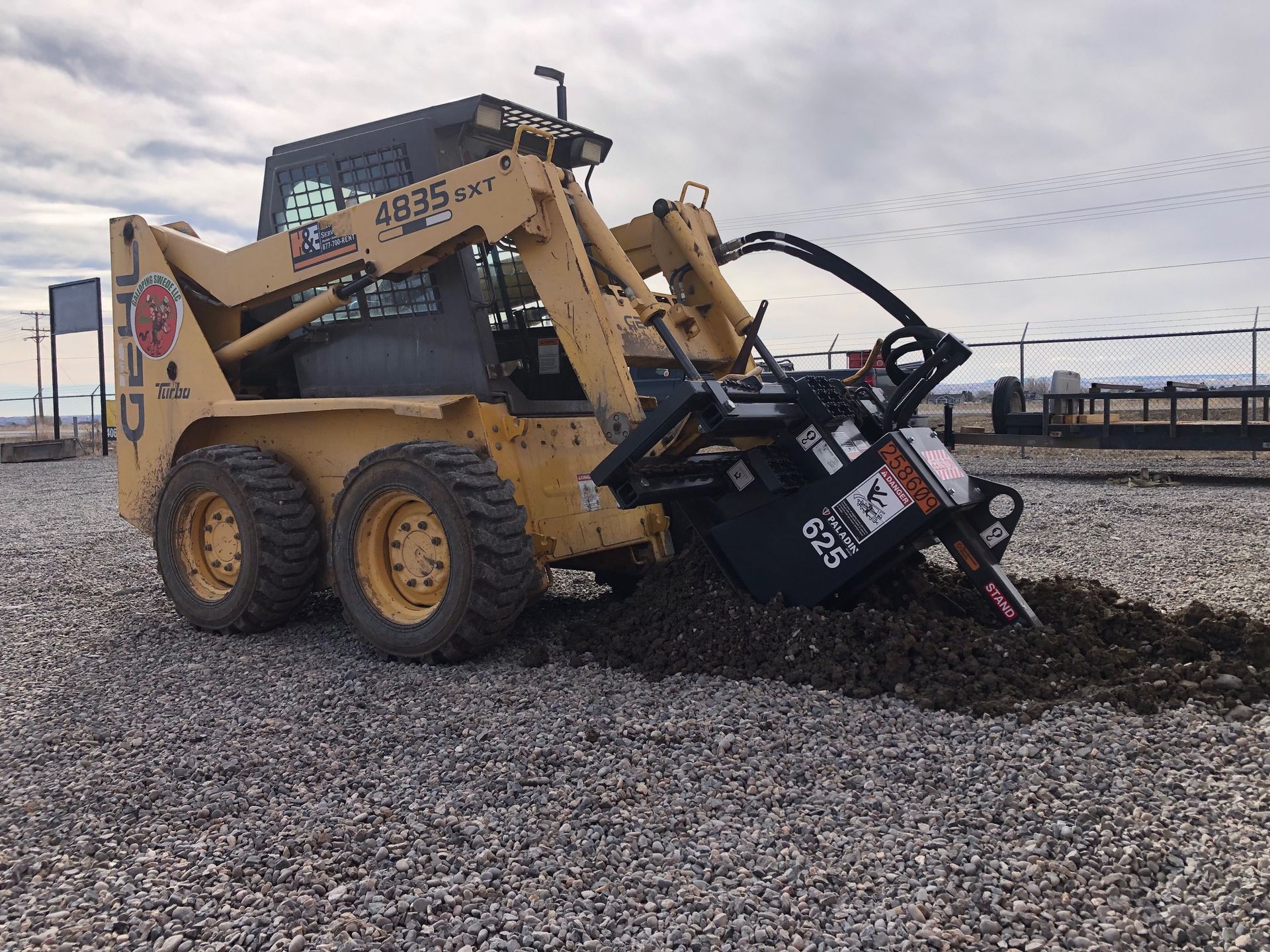 A yellow skid steer is digging a hole in the ground.