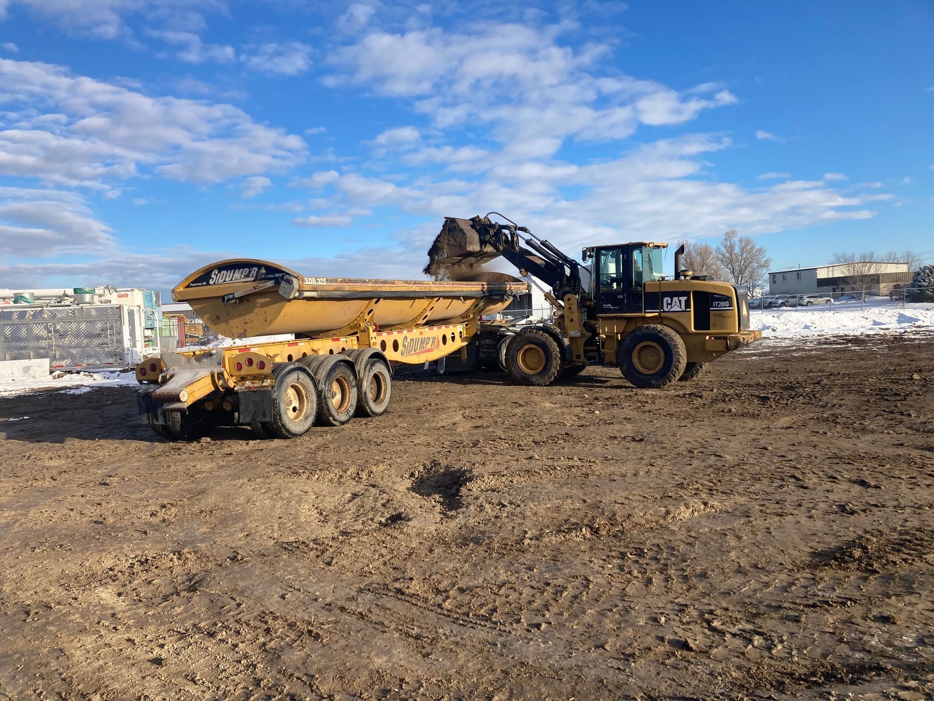 A dump truck is being towed by a bulldozer in a dirt field.