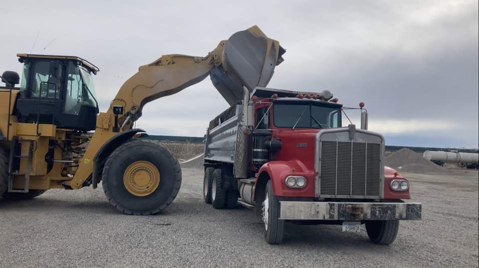 A dump truck is being loaded with gravel by a bulldozer.