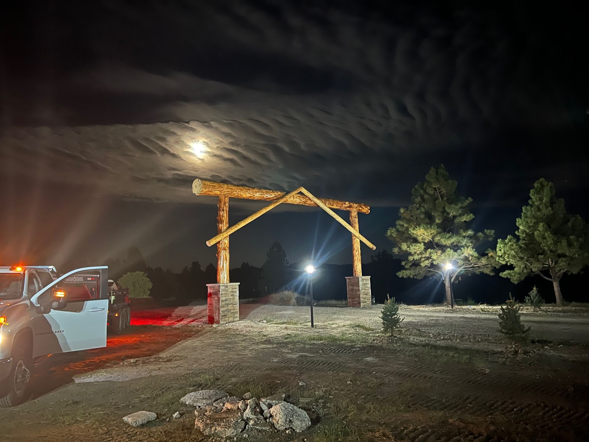 A car is parked in front of a wooden archway at night.